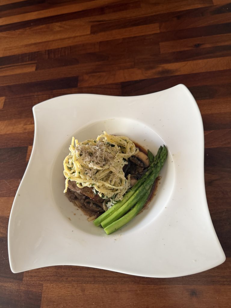 Truffle linguine with fillet steak, mushrooms and buttered asparagus on a white plate