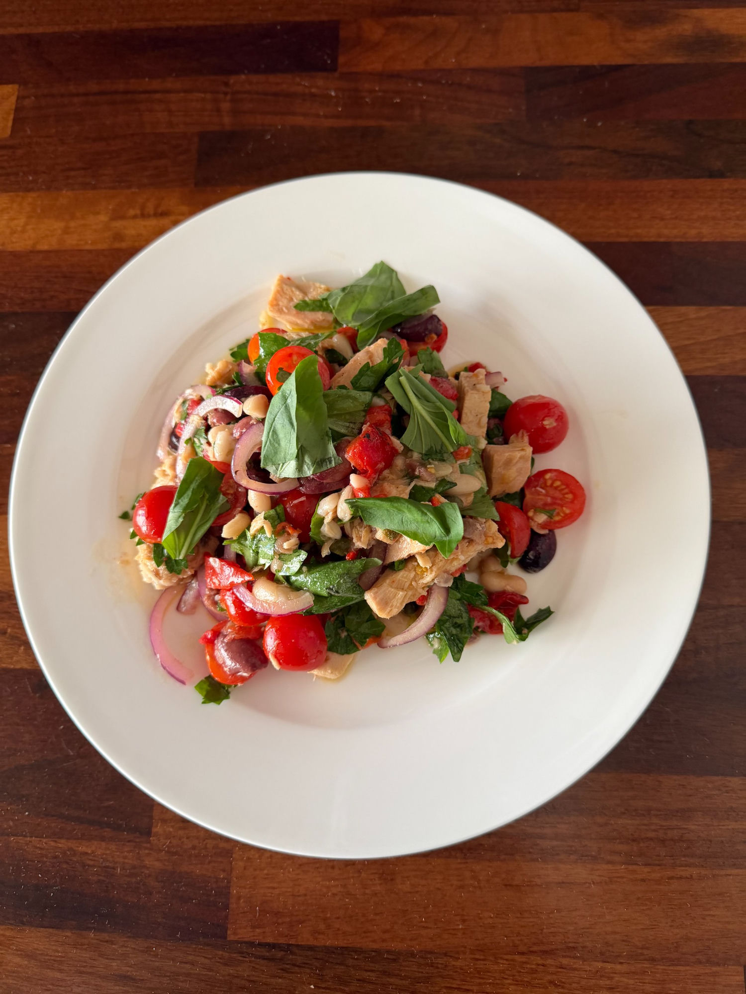 Roasted pepper, white bean and tuna salad with cherry tomatoes, red onion and basil on a white plate