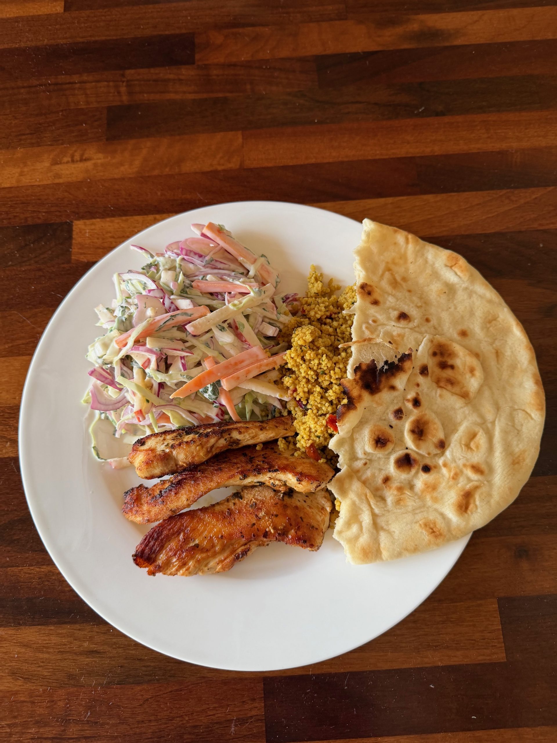 Greek chicken with tzatziki slaw, spiced couscous and warm flatbread on a white plate