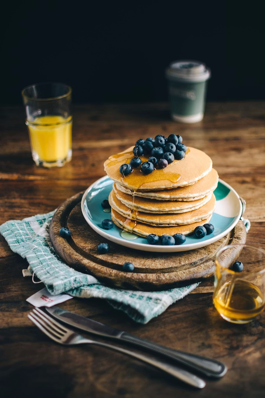 A tall stack of fluffy American pancakes topped with blueberries and maple syrup