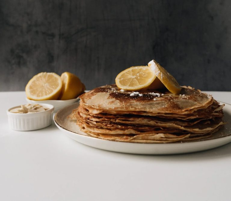 A stack of thin British pancakes with lemon slices and a dusting of sugar