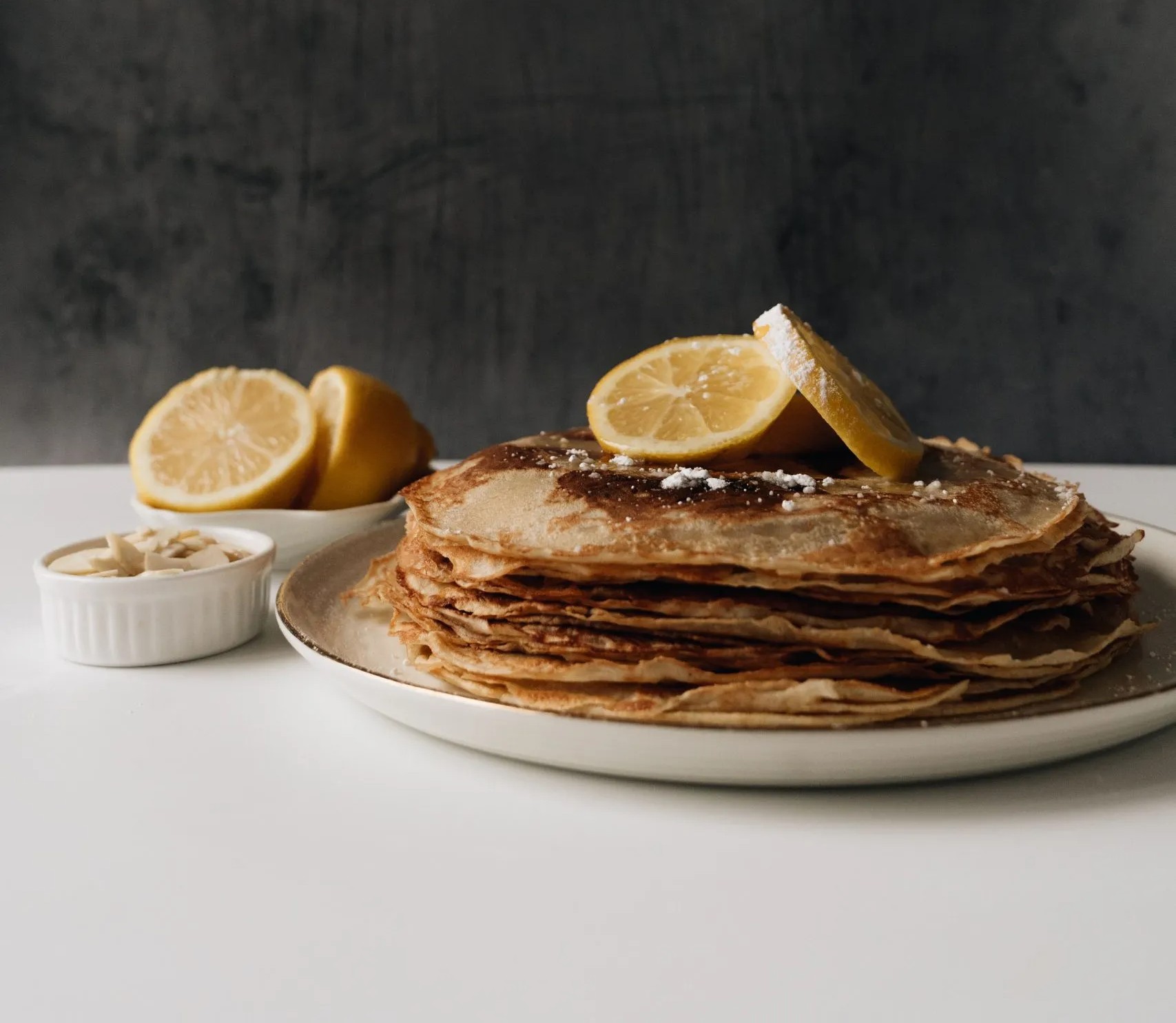 A stack of thin British pancakes with lemon slices and a dusting of sugar