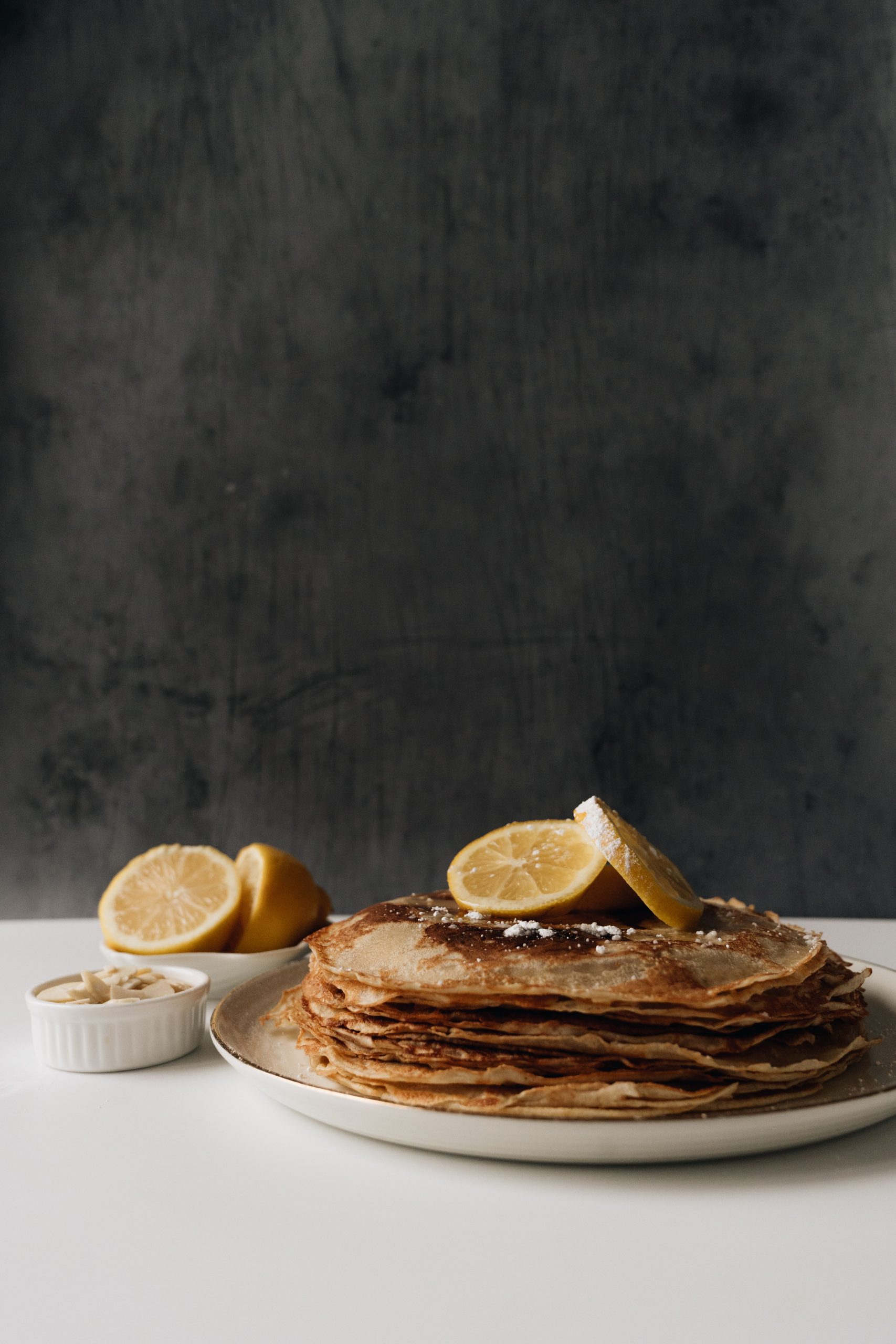 A stack of thin British pancakes topped with lemon slices and a dusting of sugar