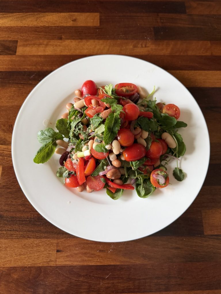 Tuscan bean salad with cannellini and borlotti beans, cherry tomatoes, red peppers and herbs on a white plate
